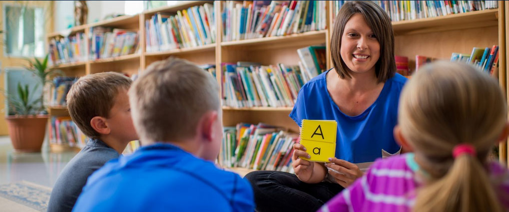 Student showing letters to young children.