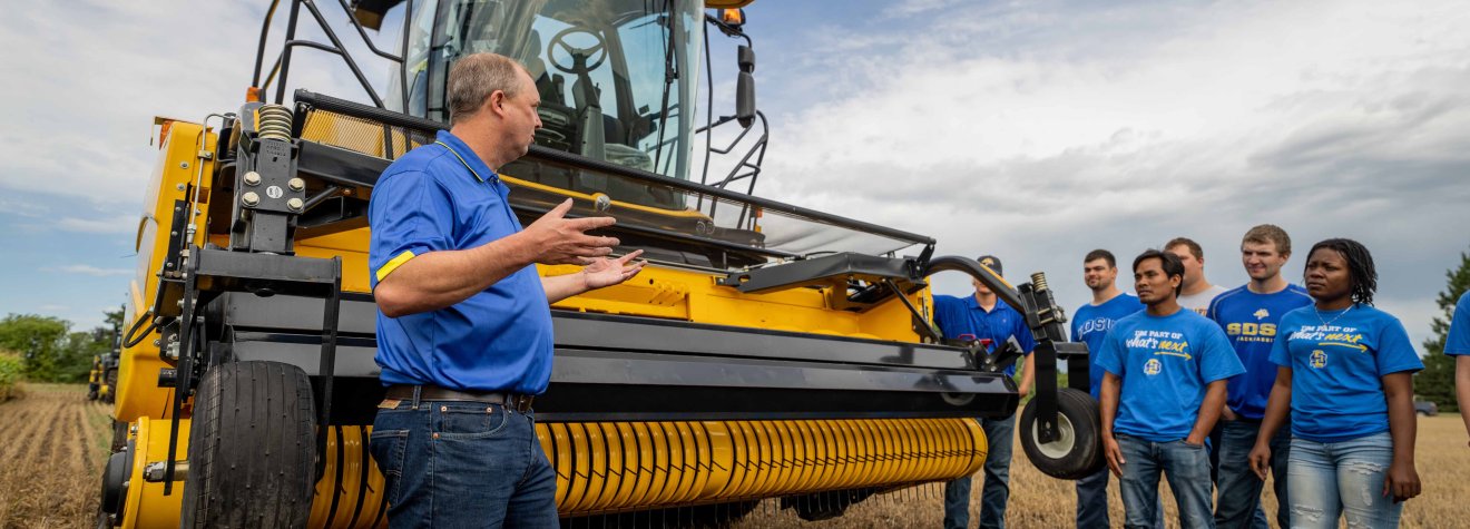 Students and instructor standing in a field next to a combine.