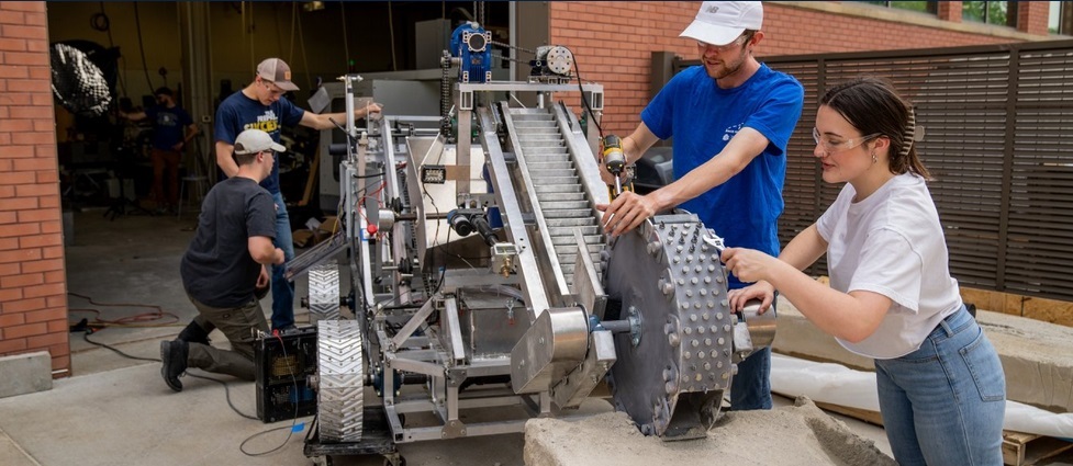 Four students standing next to a vehicle students designed and built for NASA's Break the Ice Lunar Challenge.