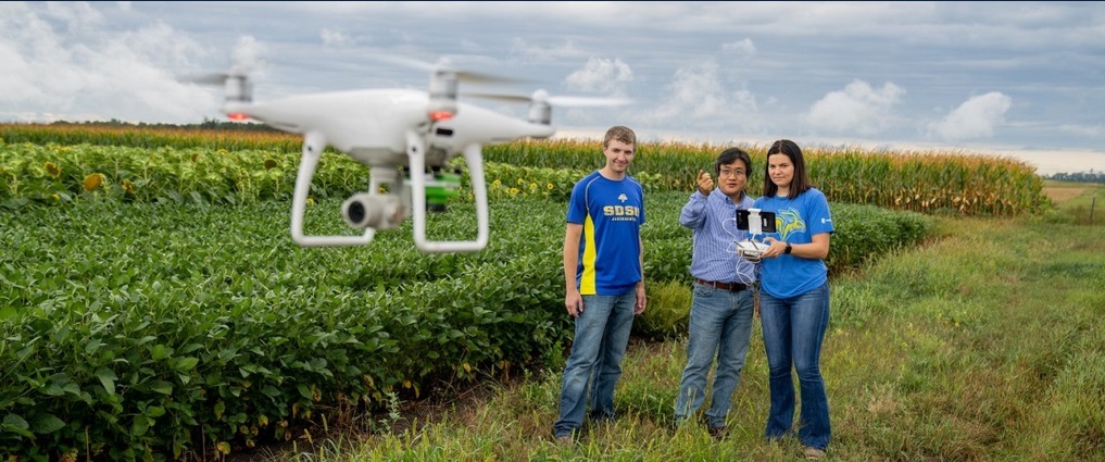 Two students and instructor flying a drone next to a field.