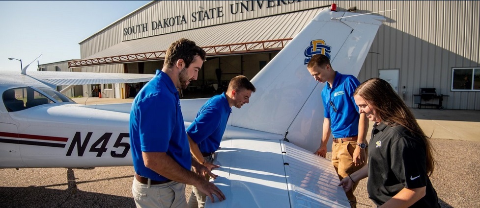 Four students standing next to a plane.