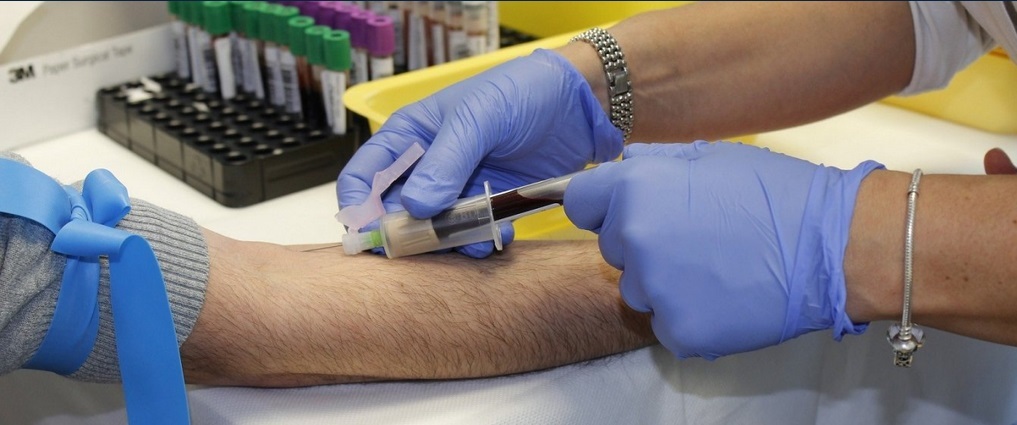 Person using a needle to draw blood from another person's arm.