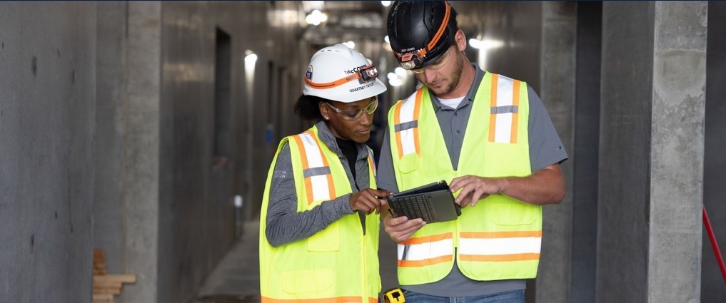 Two people on a construction jobsite looking at a computer tablet.