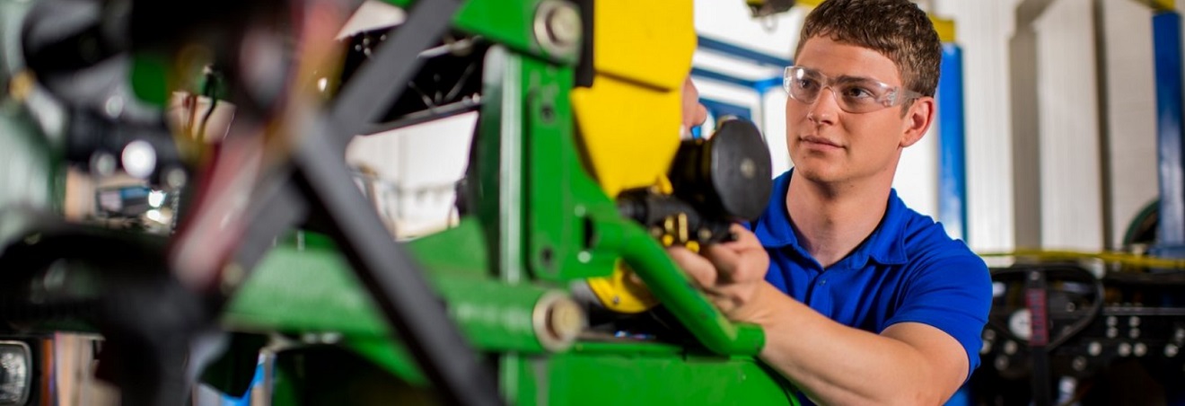 Student standing next to equipment in a shop.