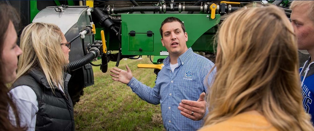 Students standing next to an instructor explaining a piece of farm equipment.