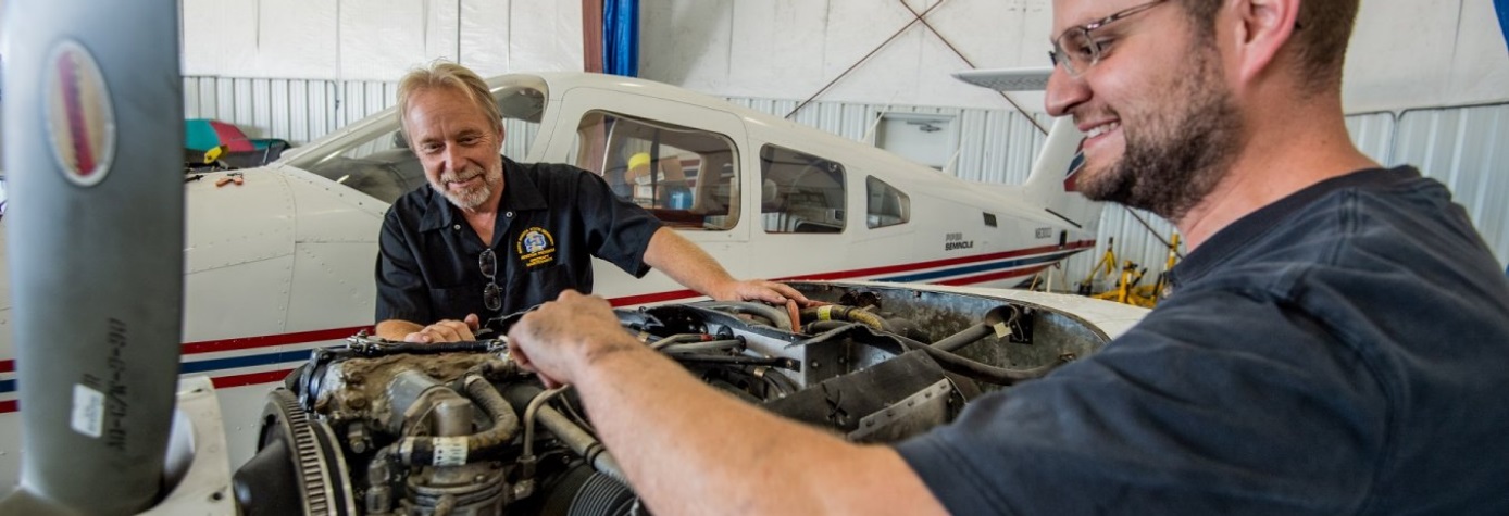 Instructor and student looking at a plane's engine.