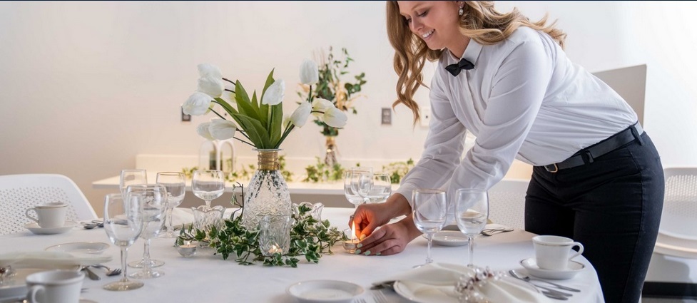 Student in white shirt and black pants decorating a dinner table.