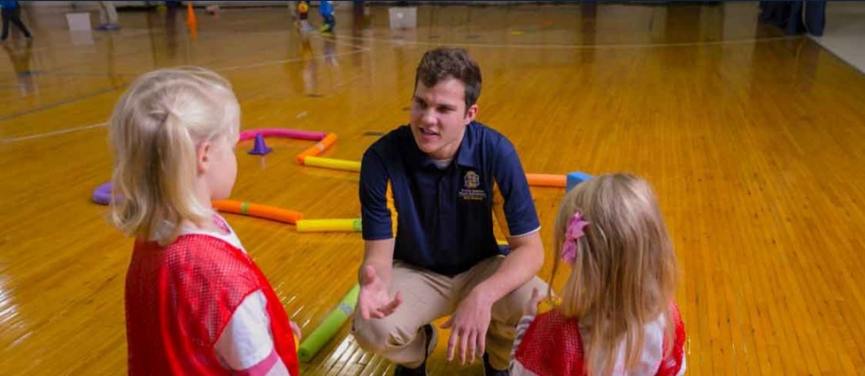 Student teacher working with young students in a gym.