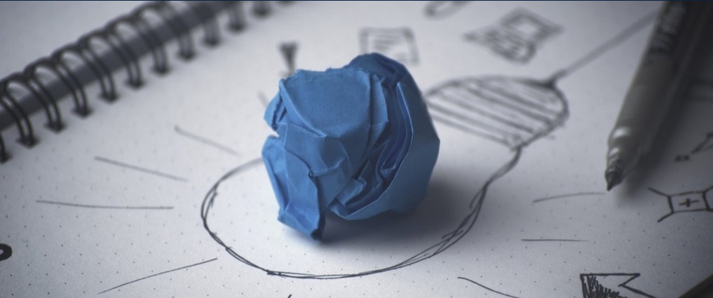 Image of a blue paper crumpled up on top of a lightbulb sketched on paper.