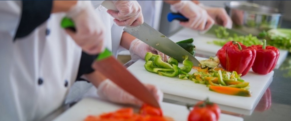 Three students in a cooking lab dicing vegetables.