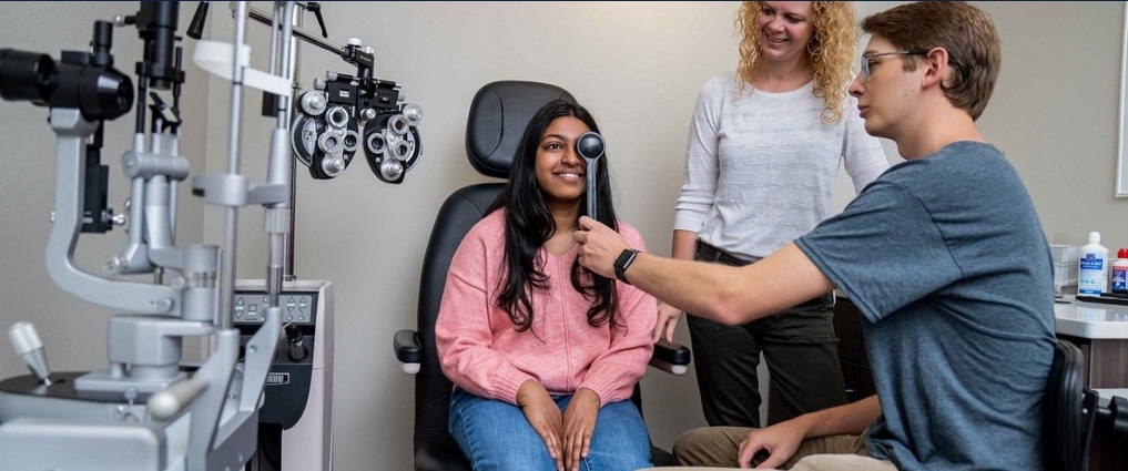 Students practicing how to give an eye exam with an optometrist watching.