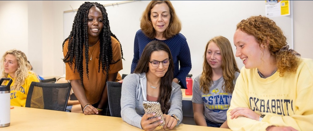 Students and professor looking at a cell phone screen,