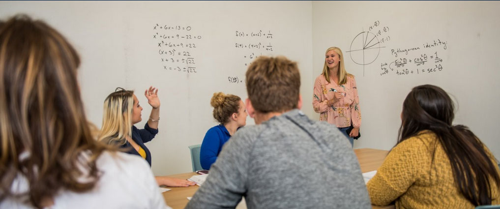 Students watching an instructor write equations on a white board.