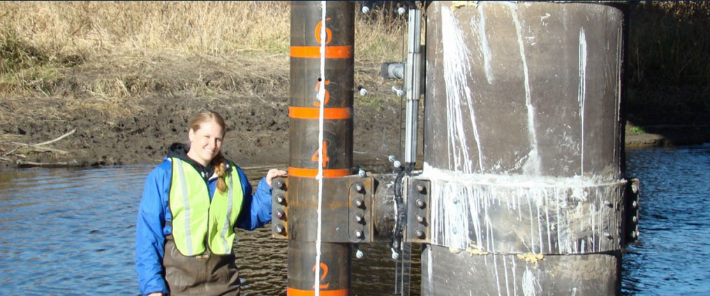 Student standing in water next to a bridge.