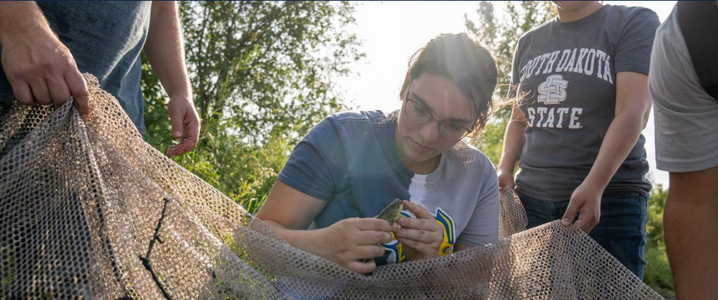 Students holding a net and a fish.