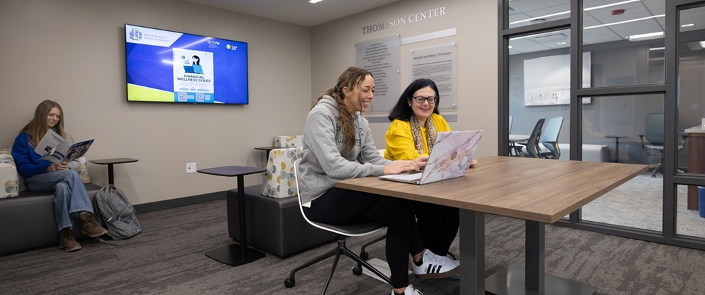 Student and professor looking at a computer with another student sitting in the background.