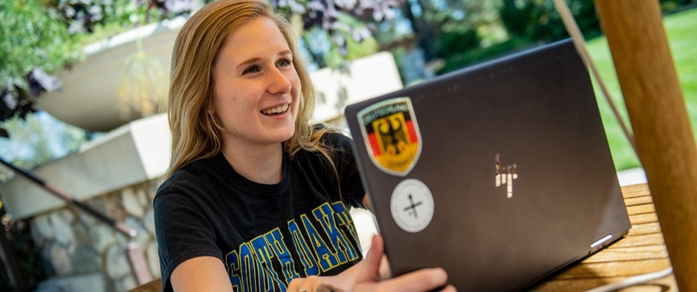 View of a student sitting outside and working on a laptop.