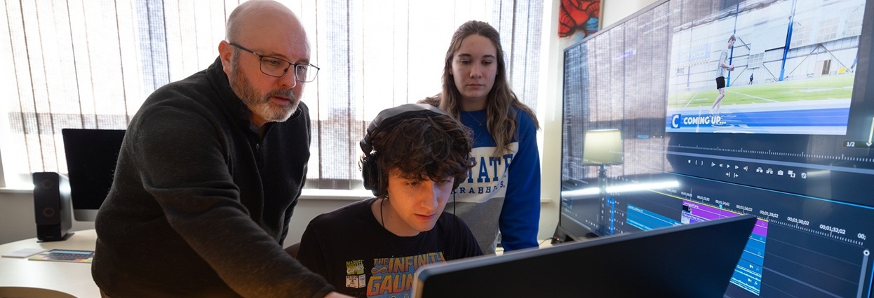 Two students and professor looking at computer monitors.