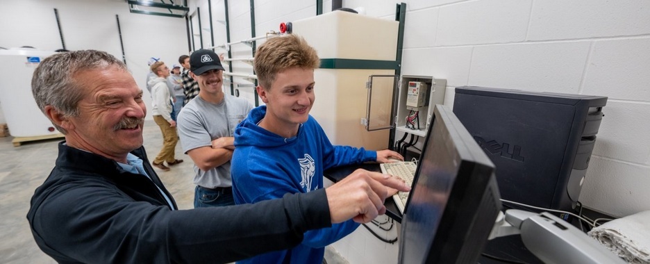 Students and professor look at a computer monitor.