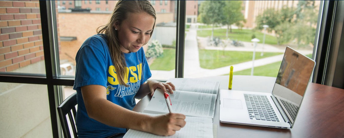 Student sitting at a table studying and writing in a notebook.