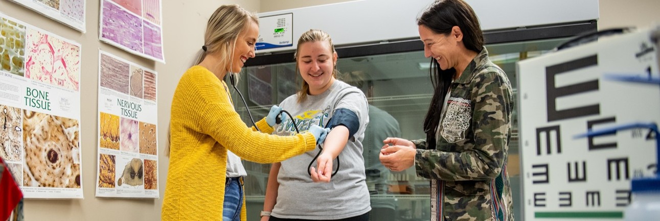 Two students practicing measuring blood pressure as an instructor observes.