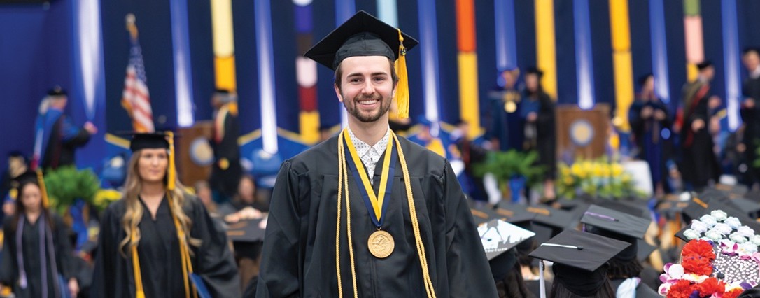 Student walking at graduation in their cap and gown.