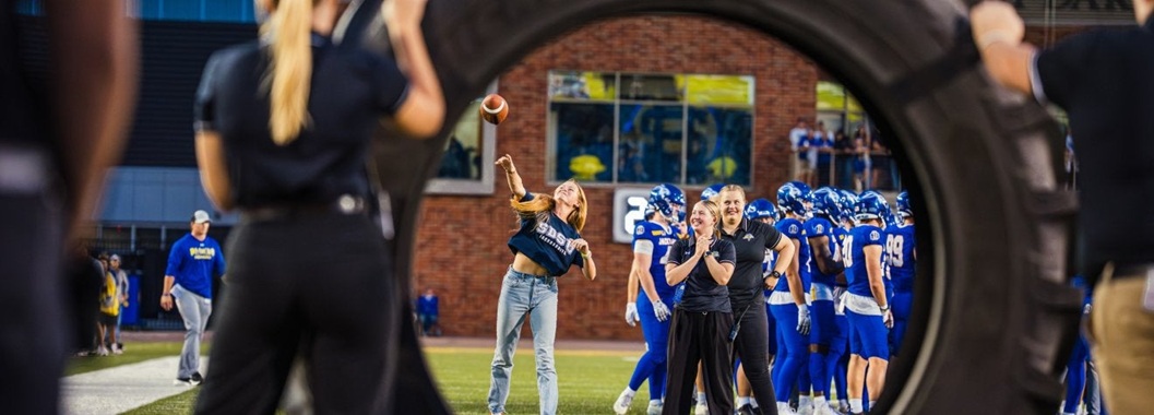 Woman throwing a football through a large tire in the football stadium 