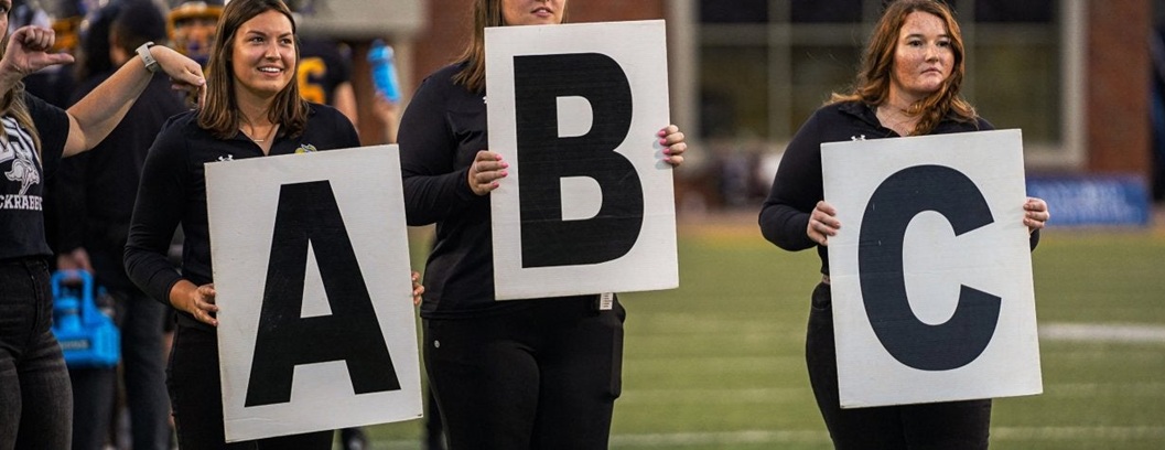Three people holding cards with the letters A, B and C for football game promo.
