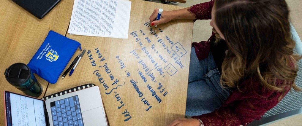 Student writing equations on a desk.