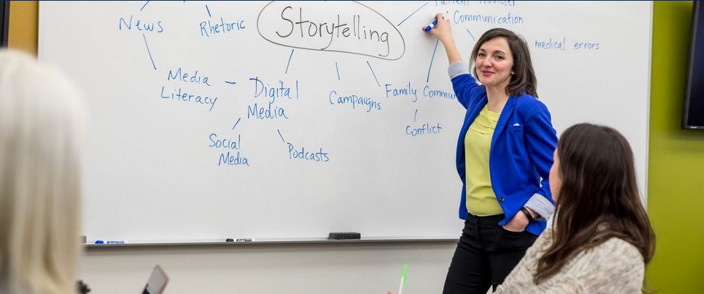 Instructor standing at a white board in front of classroom.