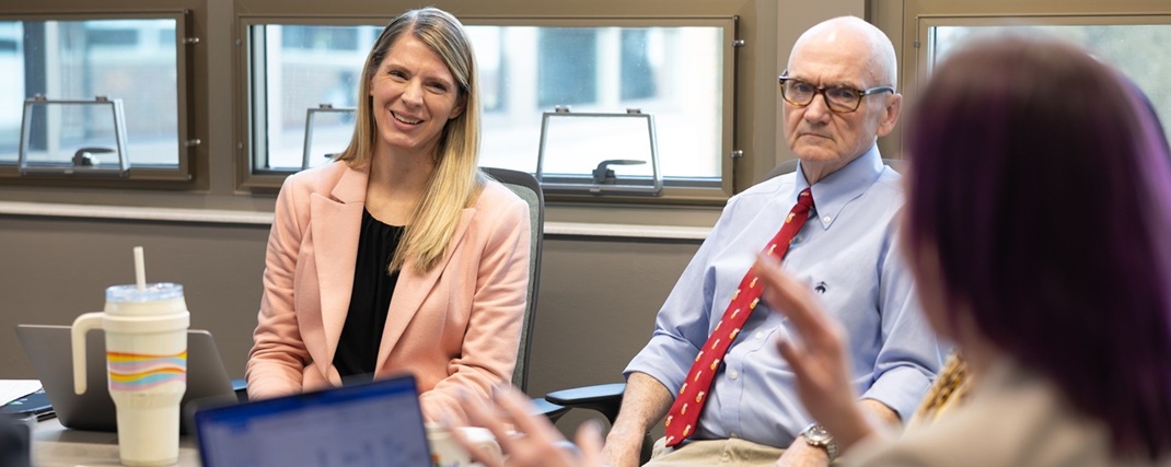 A group of four faculty sit around a table engaged in a discussion. 